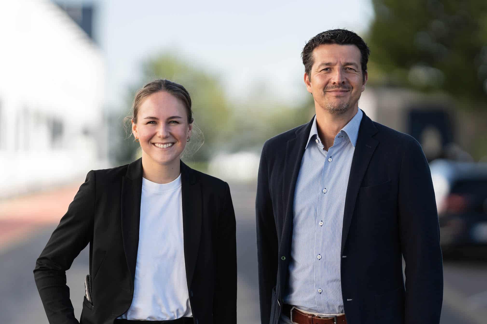 Zwei CLASSEN Mitarbeiter im Business-Outfit stehen im Freien und lächeln in die Kamera – Symbol für Professionalität, Teamgeist und Kompetenz im Unternehmen