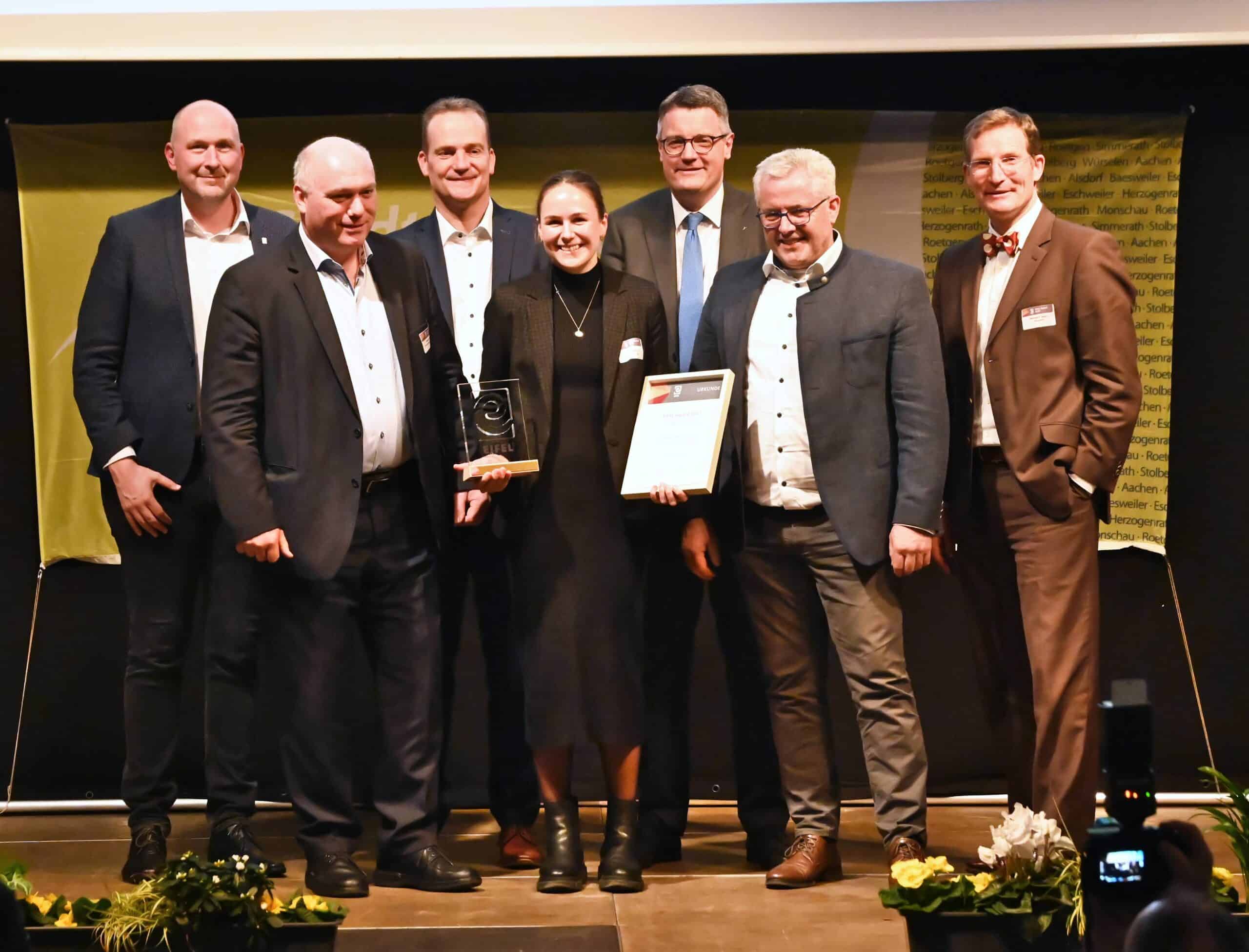 Gruppenfoto einer Preisverleihung: Mehrere Personen stehen auf der Bühne, eine Frau hält eine Auszeichnung und eine Urkunde in den Händen – Symbol für Erfolg, Anerkennung und die ausgezeichnete Leistung des CLASSEN Teams.