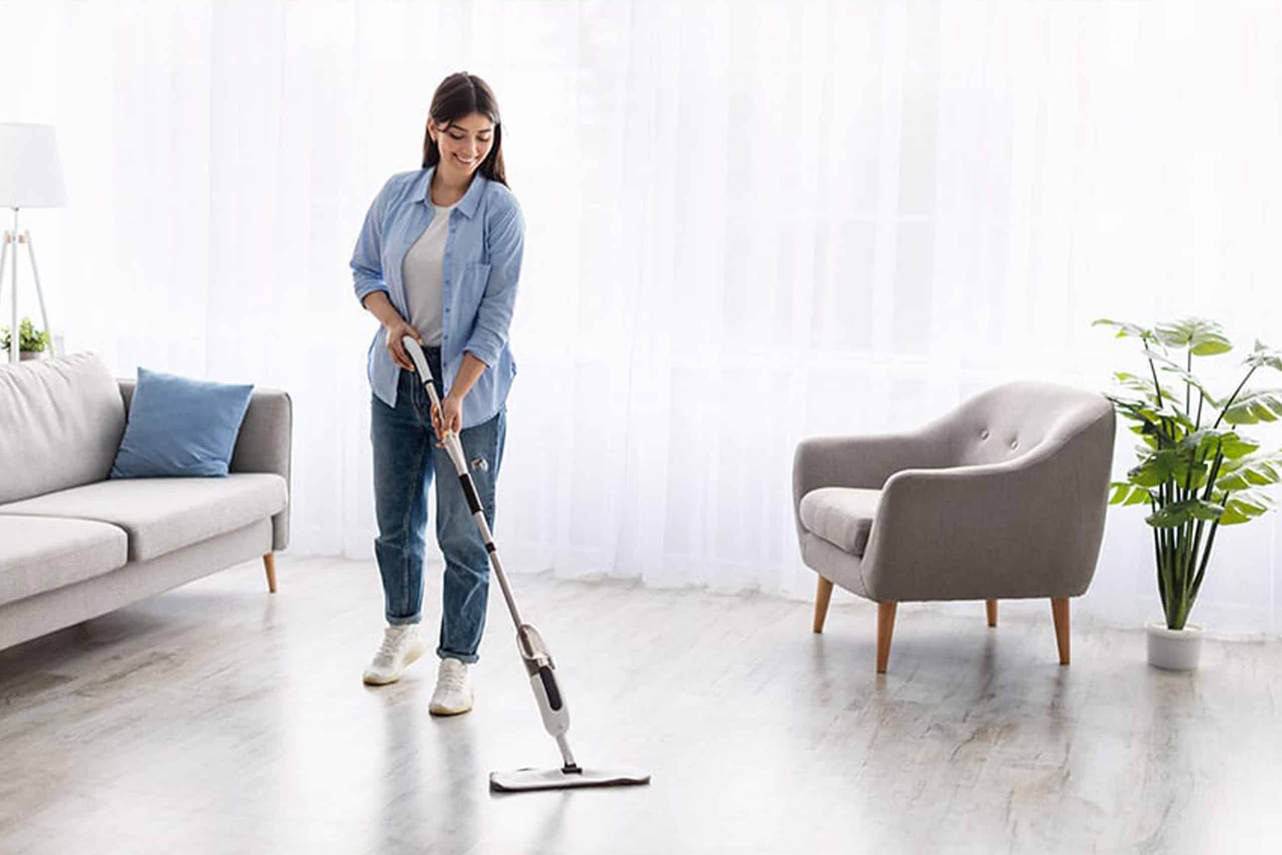 Junge Frau wischt den hellen Designboden in moderner Wohnzimmereinrichtung – pflegeleichter, strapazierfähiger Bodenbelag in Holzoptik.