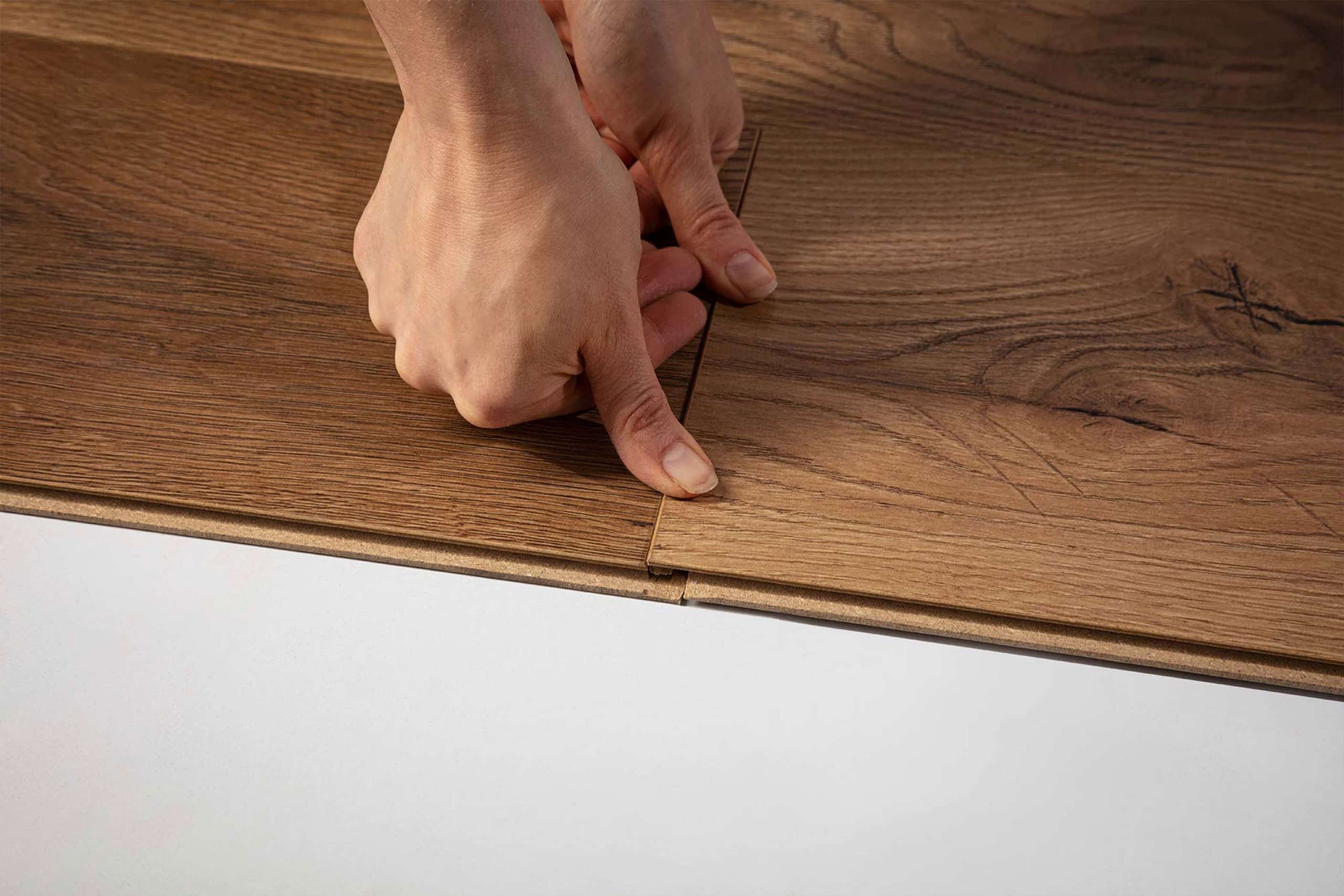 Nahaufnahme von Händen, die braune Laminatdielen mit Klicksystem verlegen – einfacher Bodenbelag in Holzoptik.