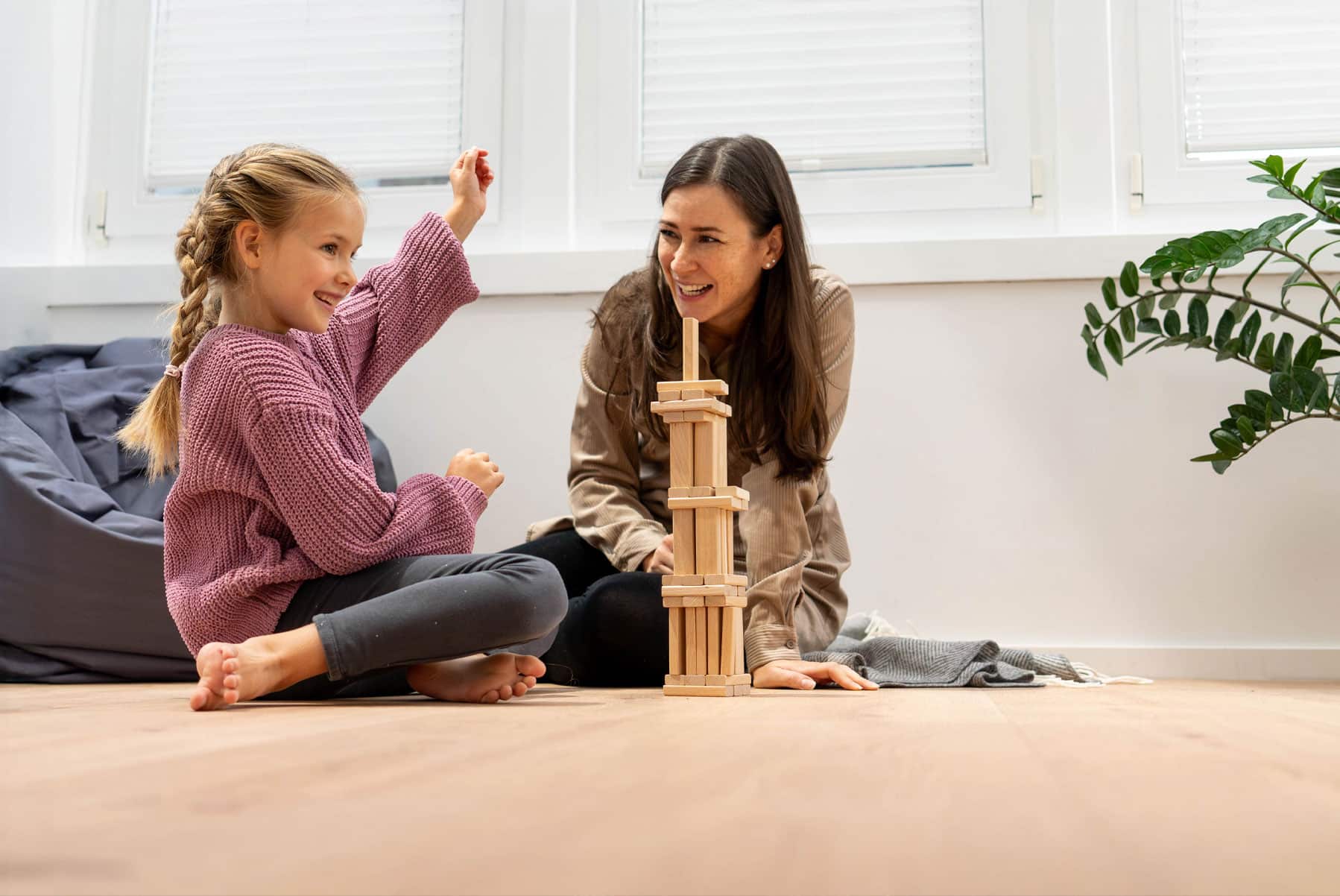Frau und Kind sitzen auf dem Boden und bauen einen Turm.